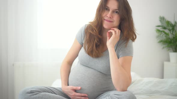 A Cute Pregnant Woman Sits in Bed