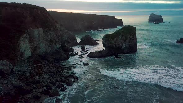 Truck left as rolling Pacific Ocean waves crash into rocky Sand Dollar Beach at dusk in Big Sur Cali