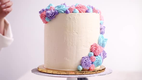 Baker piping pastel color buttercream rosettes on a white cake to make a unicorn cake.