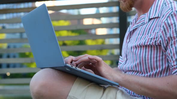 close-up of a bearded man working on a laptop against the backdrop of the city