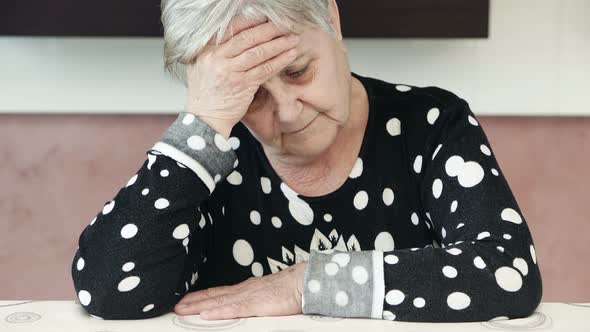 old woman shakes her head in disbelief sitting in her kitchen