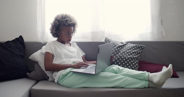 African American Woman Working at Home Lying on the Sofa with a Laptop