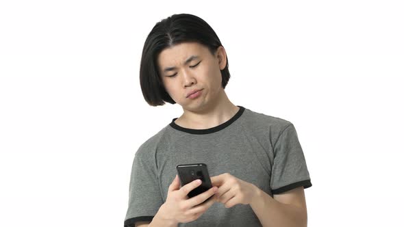 Portrait of Smiling Chinaman with Clean Skin in Casual Gray Tshirt Using Cell Phone and Scrolling