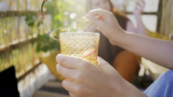 Close Cocktail Glass in Hand Against Blurry Woman on Terrace