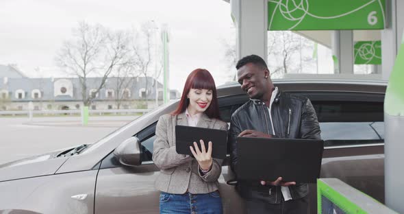 Male And Female Business People Using Tablet And Laptop Near Their Car Shooting