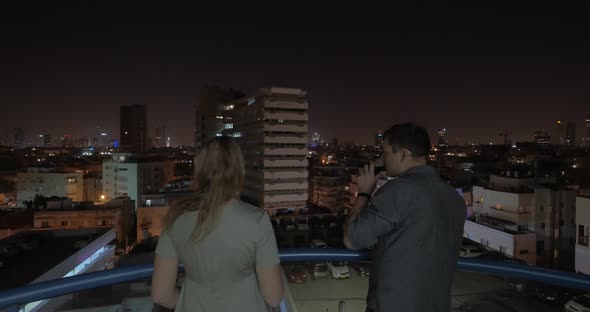 Man and woman looking at night Tel Aviv from the hotel roof, Israel