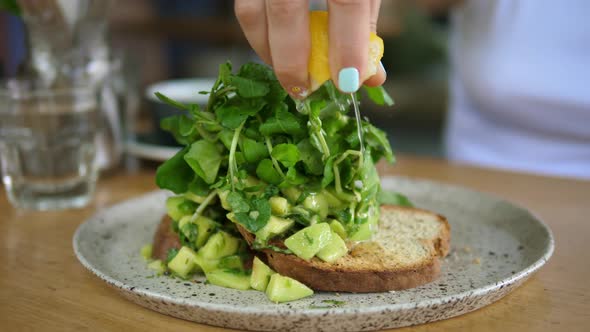Close Up of a Woman Squeezing Lemon on the Avocado Toast with Green Leaves in the Cafe on Healthy