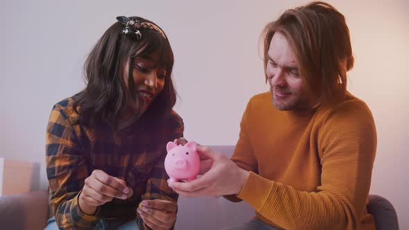 Happy Young Multiracial Couple Putting Coins in the Piggy Banks Saving Money for Their New Home