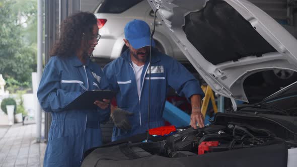 Mechanic man and woman in uniform checking diagnostic for fix and repair car together at garage.