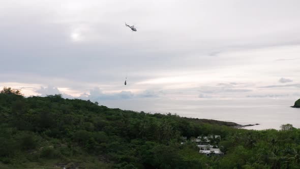 Helicopter flying away with supplies hanging from rope at remote island, aerial