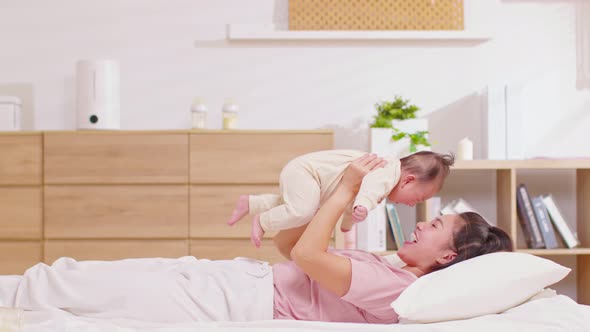 New asian mom playing to adorable newborn baby on bed smiling and happiness at home