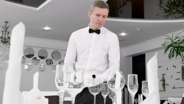 Male Waiter in White Gloves Pours Red Wine Into a Glass