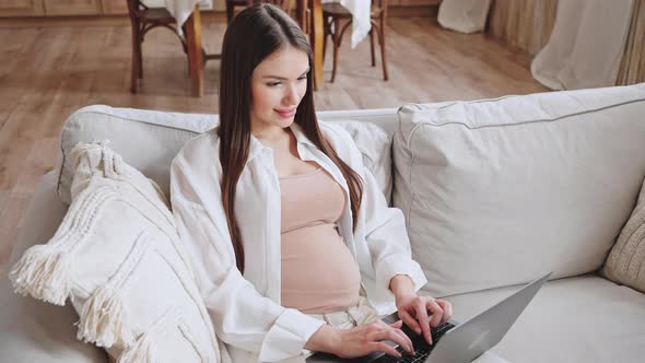 Pregnant Woman Works on Laptop Sitting on Couch at Home