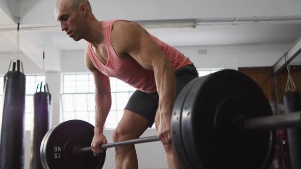 Caucasian male trainer working out with barbell at the gym