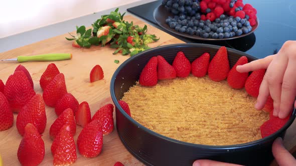 A Woman Puts Strawberries on the Bottom of a Cake Base Made of Cookie Crumbs in a Form - Closeup