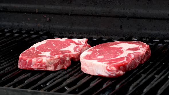 Two raw rib-eye steaks getting ready to cook on a grill.