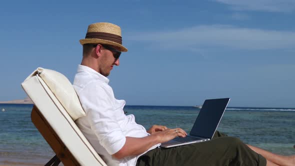 Young Man Using Laptop Computer Relaxing On The Beach.