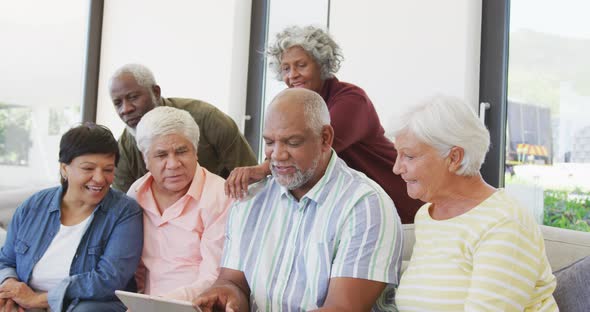 Happy senior diverse people talking and using tablet at retirement home