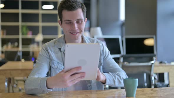 Cheerful Young Male Designer Doing Video Chat on Tablet in Office