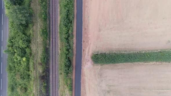 Top down aerial tracking forward along a train track and a road in the countryside, with a heavy mac