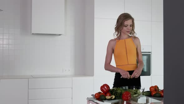 A Young Woman Is Preparing A Vegetable Salad. White Modern Kitchen.