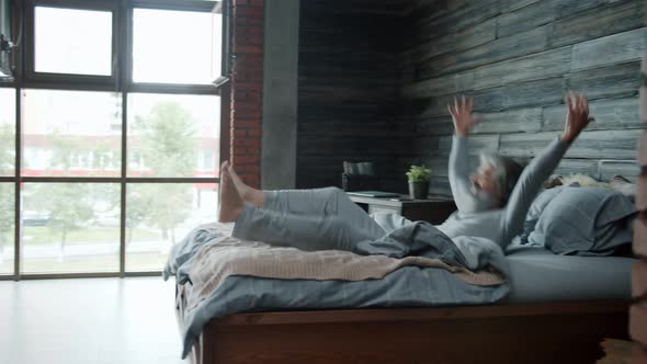 Slow Motion of Mature Man Wearing Pajamas Jumping in Bed at Home Enjoying Rest Alone