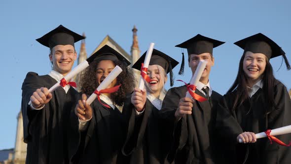 Smiling Graduates Posing in Single Line with Diplomas