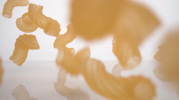 Camera follows dried macaroni pasta falling on surface. Slow Motion.