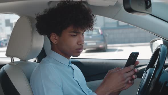 Portrait of Black Man Browsing Smartphone is Sitting a Car Sunny Day in Parking