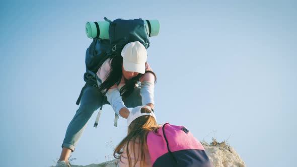 Girl Helps Her Friend Climb Up the Last Section of Mountain. Tourists with Backpacks Help Each Other