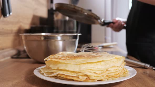 Stack of Pancakes on the Background of an Unrecognizable Woman Pouring Dough Into a Frying Pan