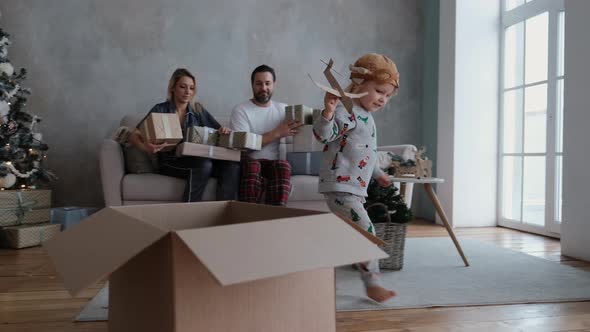 Little Finger Plays Pilot with Cardboard Plane in Hand Happy Parents Are Watching the Child at