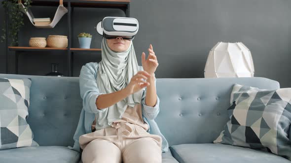 Young Muslim Lady Moving Hands Wearing Virtual Reality Glasses at Home Having Fun