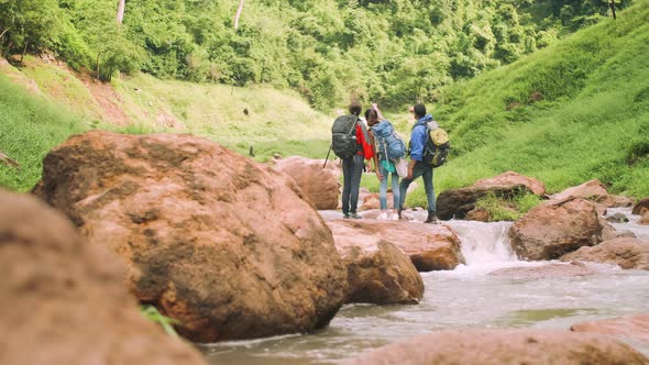 A group of trekkers with backpacks standing on the rock of a stream in a green valley.