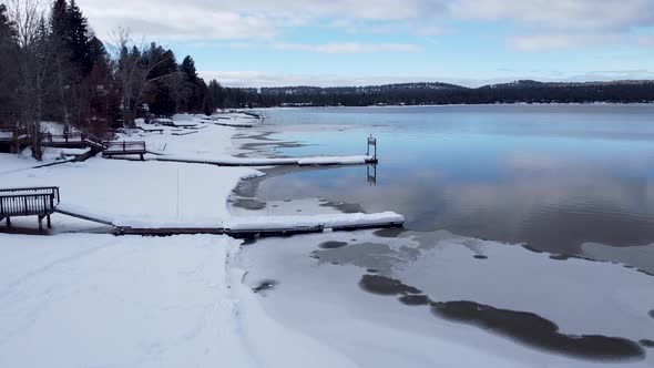 Snowy icy frozen lake in winter with empty snow covered boat wharf jetty at lake front houses in McC