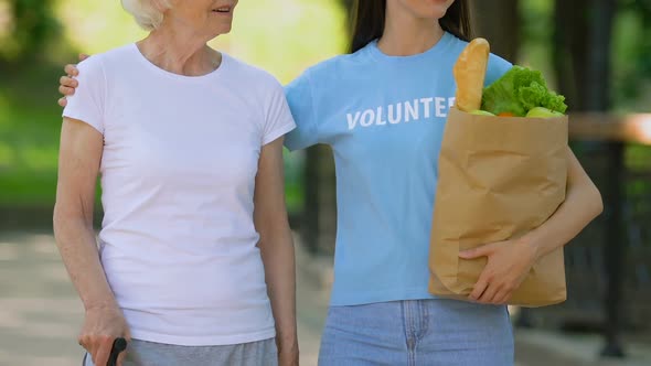 Volunteer Bringing Food to Old Disabled Lady With Cane, Walking in Hospital Park