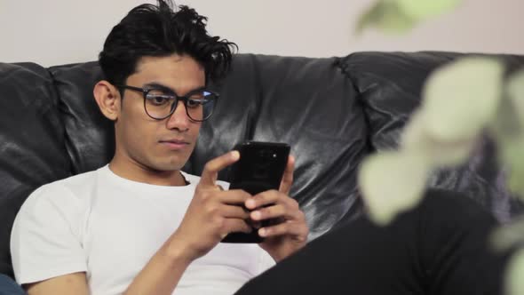 Handsome young man with glasses sitting on couch and typing, close up view