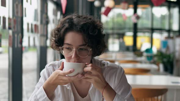 Close Up Portrait Of A Young Curly Haired Girl, A White Girl Sits In A Restaurant Drinks Coffee, Cup
