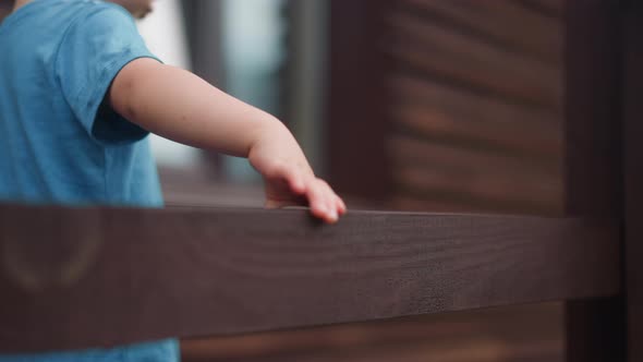 Toddler Boy Touches Wet Beam of Handrail Walking on Veranda