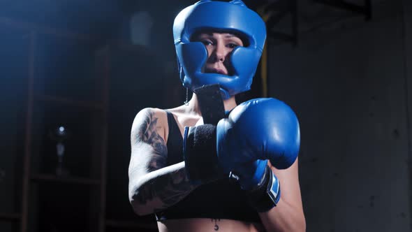 Tattooed Woman in Protective Soft Helmet Puts on Boxer Gloves and Stands in the Fight Pose