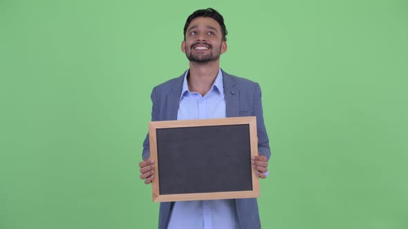 Happy Young Bearded Persian Businessman Thinking While Holding Blackboard
