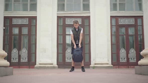 Wide Shot of Joyful Schoolboy Spinning with Rucksack After Classes Outdoors. Portrait of Happy