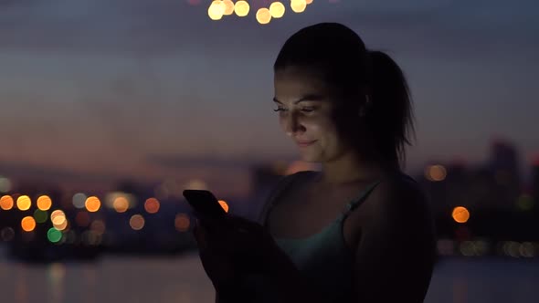 A Girl is Using a Smartphone in the Background of a Night City