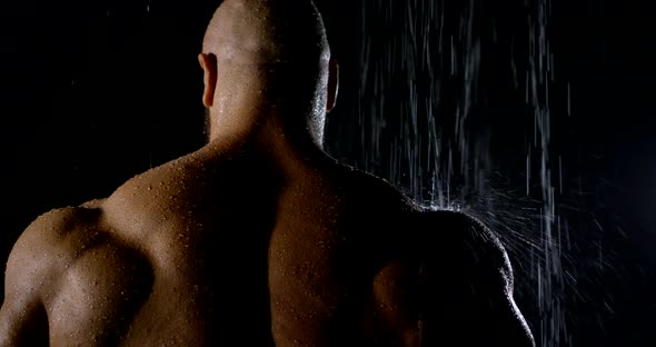 Big Muscular Jock Is Standing in Shower Under Water Stream, Back View in Darkness