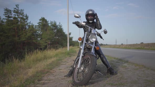 Front View of the Successful Confident Young Woman in Leather Dress Sitting on Her Bike at the Road