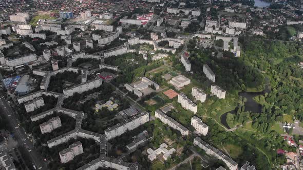 Aerial View of Geometrically Shaped Buildings in a City Surrounded by Trees Pan Down