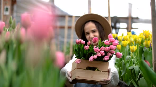 Young Girl Gardener in a Hat Holds Out a Wooden Box with Bouquets of Tulips Closeup