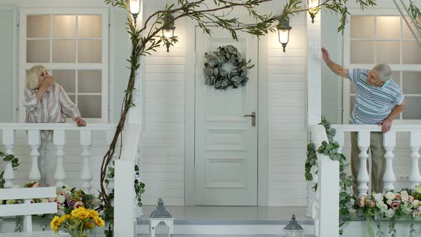 Senior Elderly Couple Waving Hands Each To Other, Making Air Kisses While Staying in Porch at Home