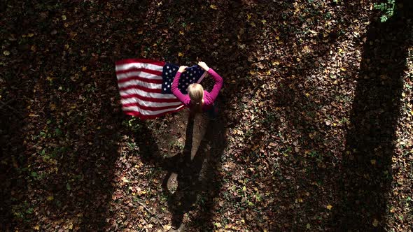 Looking straight down as a woman spins and whips an American flag around in a forest.