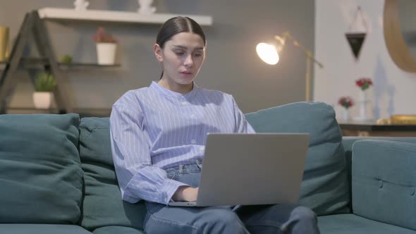 Hispanic Woman with Laptop Reacting to Loss on Sofa